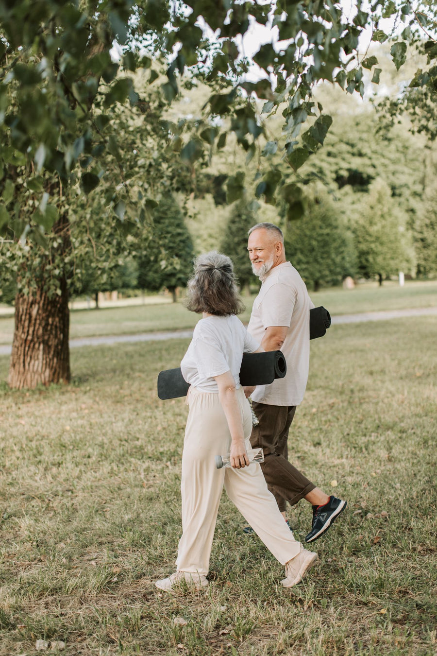 Older couple walking through a green park carrying yoga mats