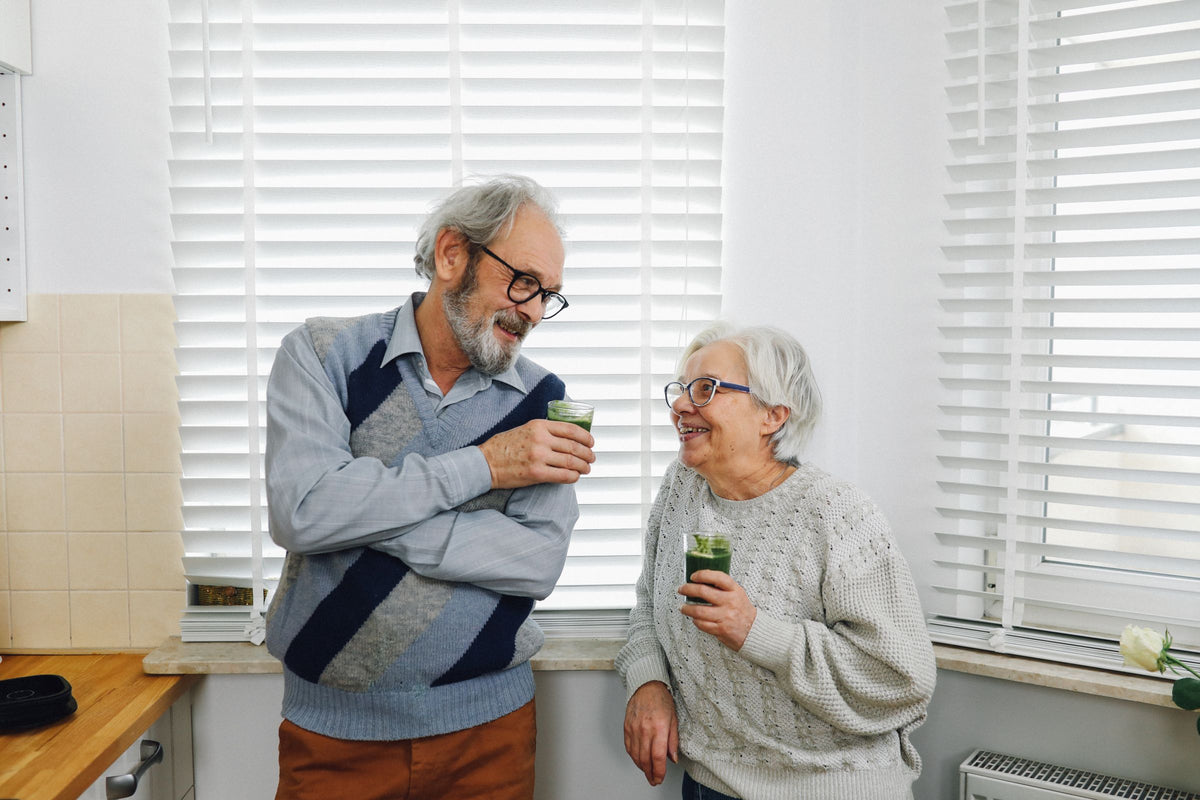 Older couple smiling together with fresh green drinks in a bright kitchen